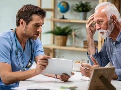 Worried senior patient and his doctor using touchpad during medical appointment.